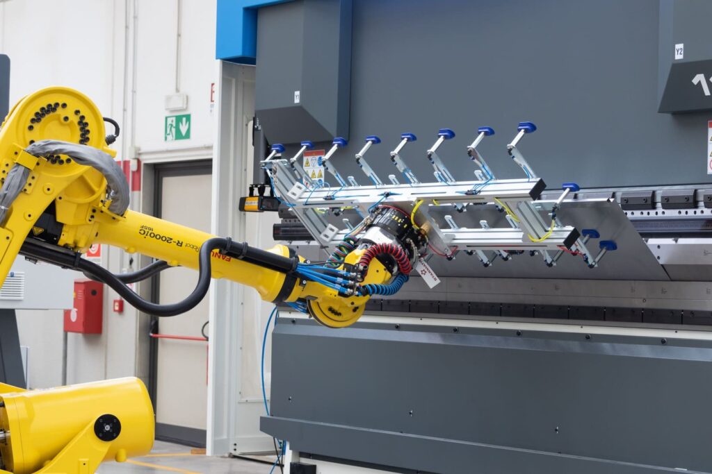 Célula de plegado automatizada: un robot FANUC con ventosas carga una plancha de acero en la plegadora industrial.