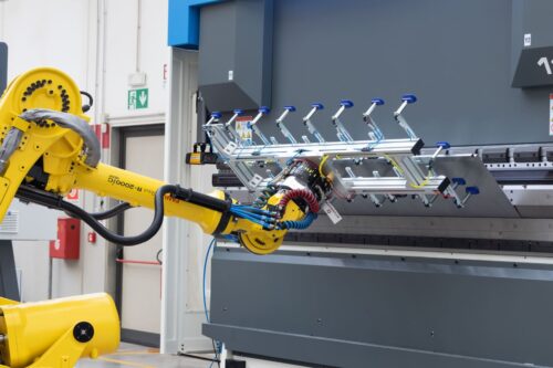 Célula de plegado automatizada: un robot FANUC con ventosas carga una plancha de acero en la plegadora industrial.